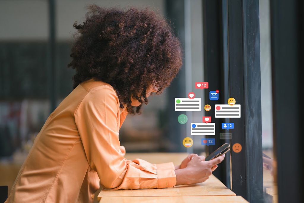 Smiling african american businesswoman engaging with social media on smartphone at modern workspace - JoberTalk social media brand marketing